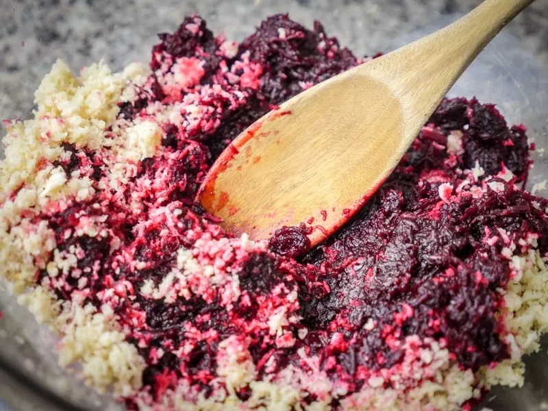 A wooden spoon mixing beets and horseradish together in a glass bowl