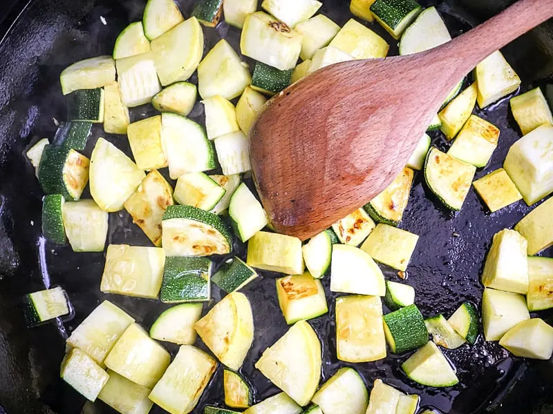 Overhead shot of zucchini and yellow squash cooking in a cast iron skillet.
