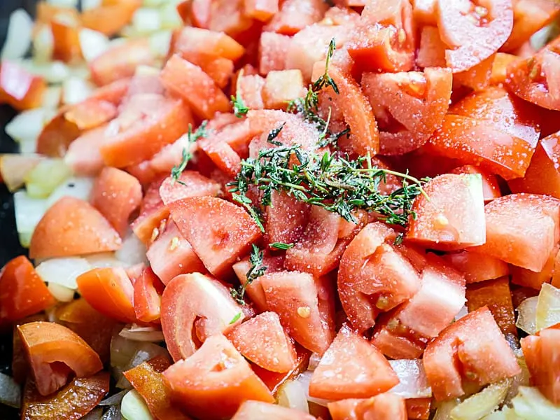 Close up of diced tomatoes and thyme in skillet.