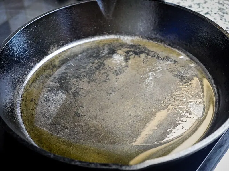 Image of olive oil heating in a large cast iron skillet.