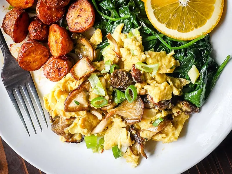 Image of oyster mushrooms over scrambled eggs on a white plate.