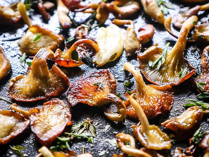 Close up of butter, garlic, and thyme with crispy oyster mushrooms in a cast iron skillet.