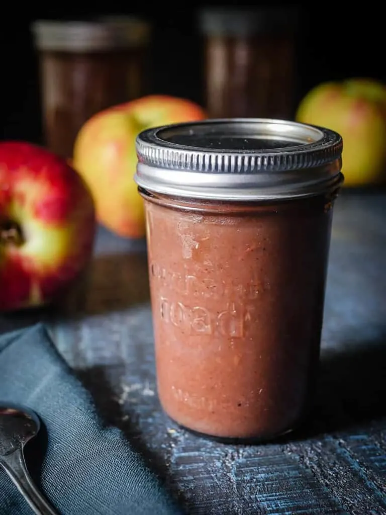 Side shot of canned Instant Pot Apple Butter on a blue wooden table.