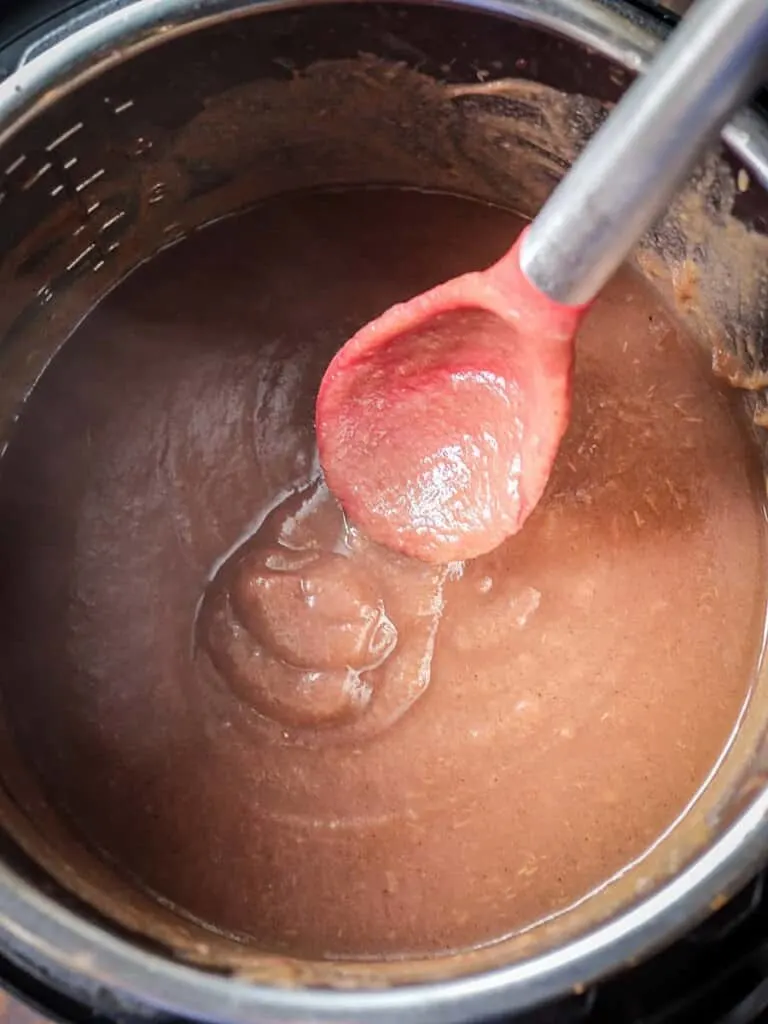 Overhead shot of reduced apple butter in an Instant Pot with a spoon.