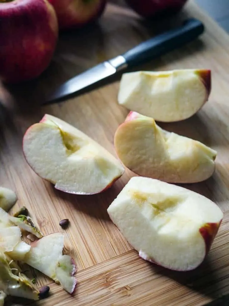 Close up of a quartered apple on a wooden cutting board.