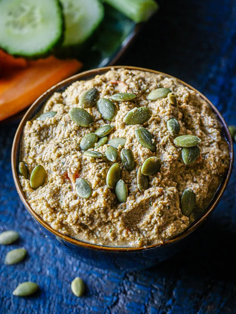 Shot of Sikil Pak Pepita Dip in a blue bowl along side cut vegetables.