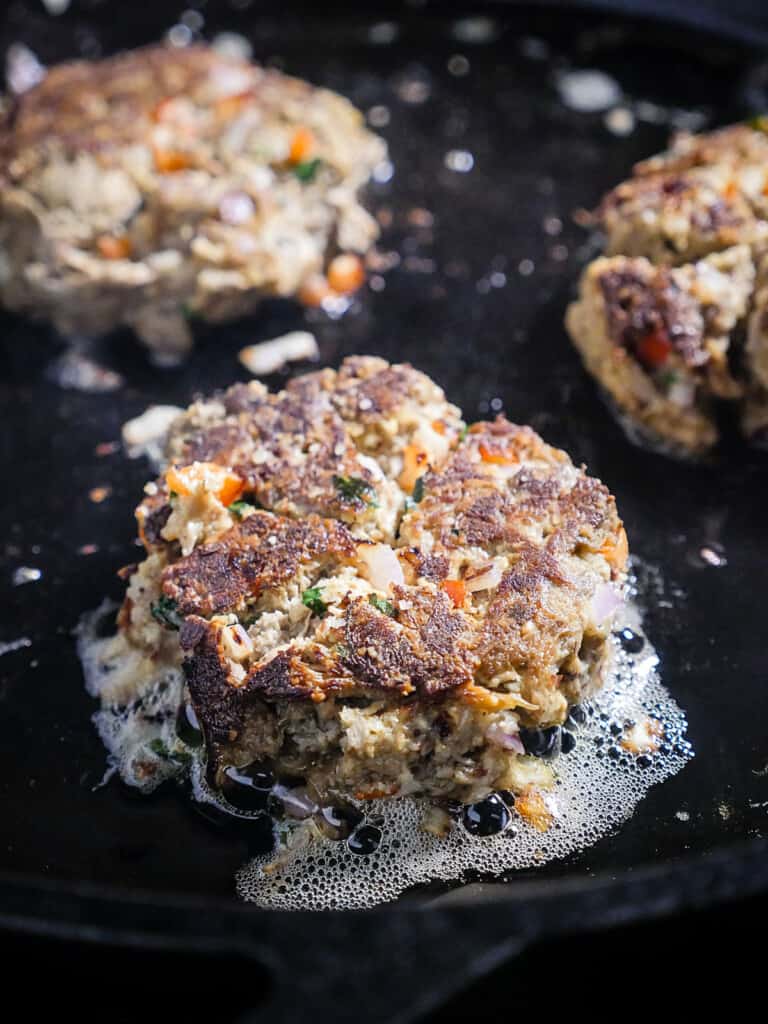 Close up of frying Lion's Mane Crab Cakes in avocado oil in a cast iron skillet