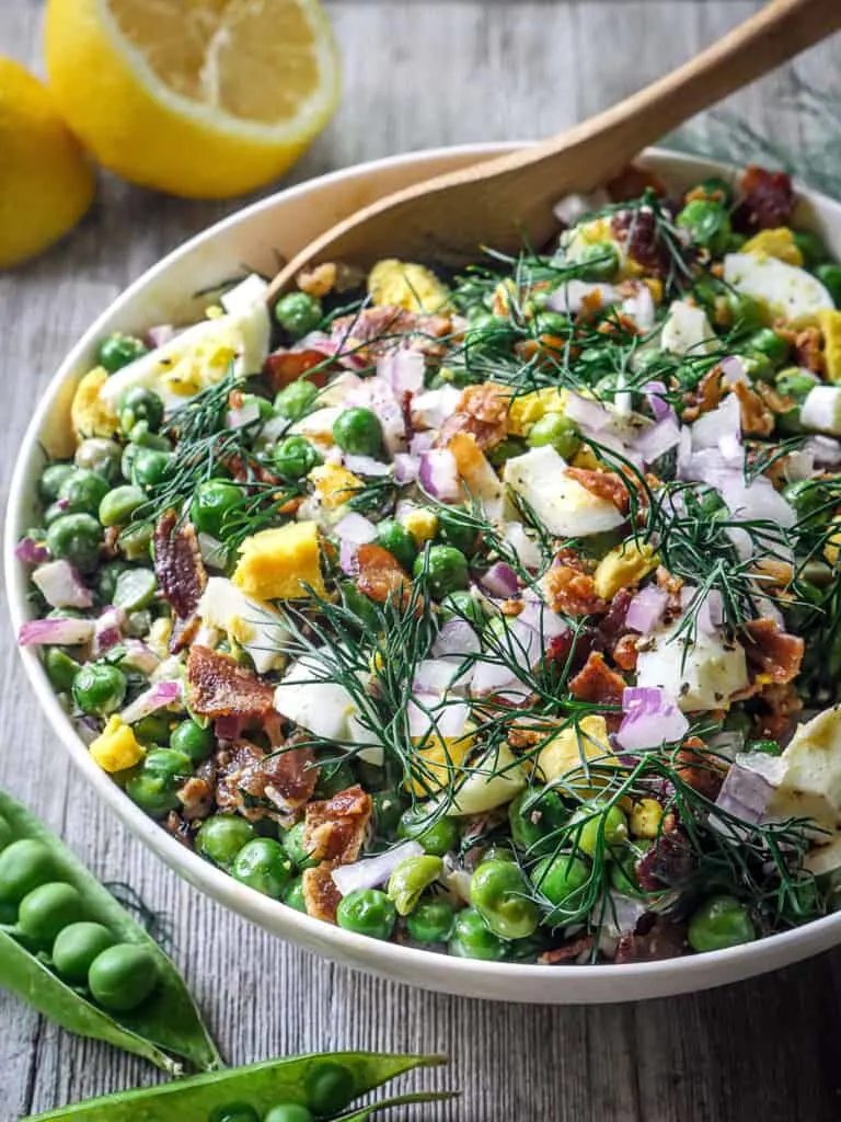 Close up of Whole30 English Pea Salad in a white bowl on a grey wooden background.