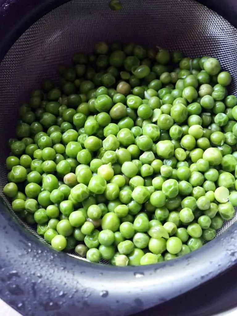 Close up of cooked English peas in a metal strainer.