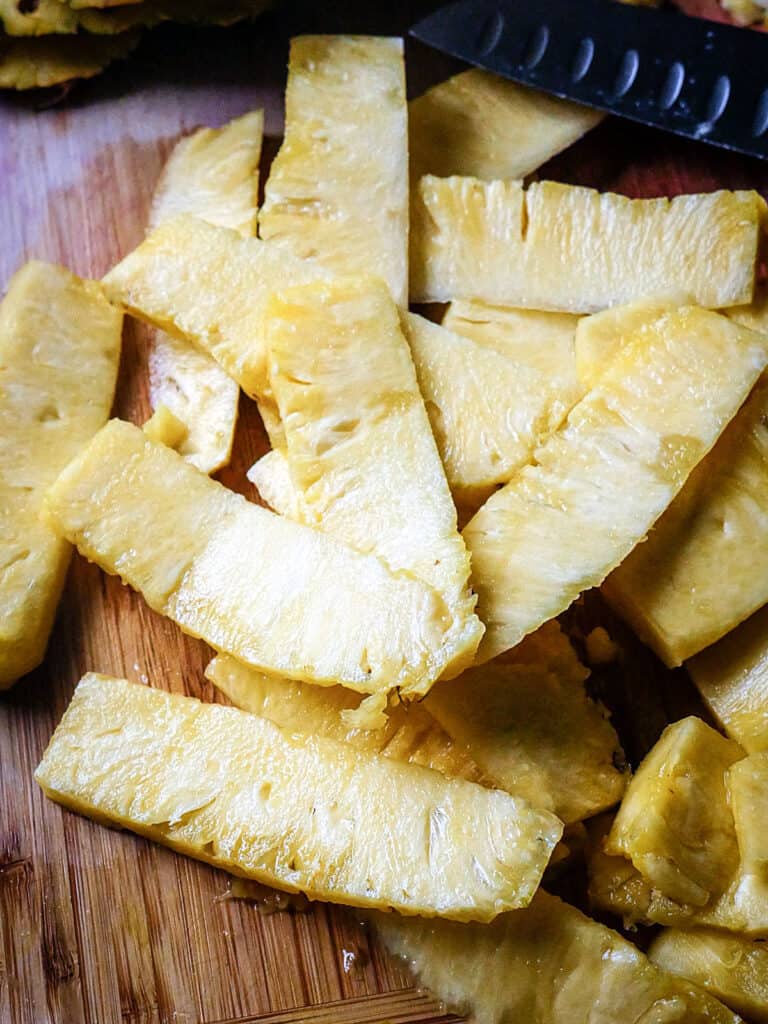 Close up of pineapple slices on a wooden cutting board.