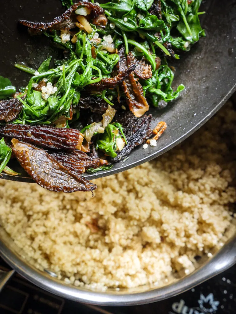 Morel mushroom mixture being added to a pot of quinoa.