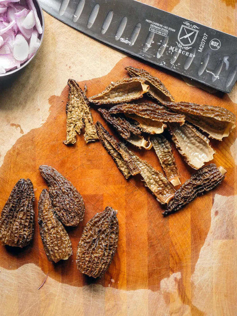 Rehydrated morel mushrooms sliced on a wooden cutting board.