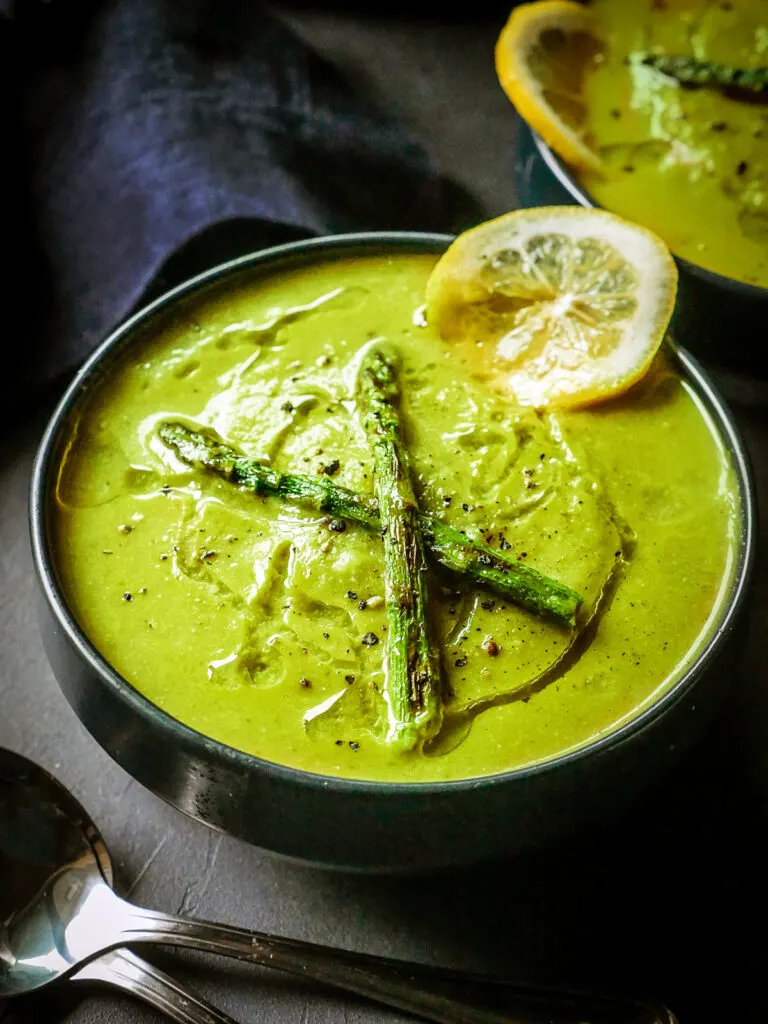 Moody image of dairy-free Cream of Asparagus soup in a dark bowl.