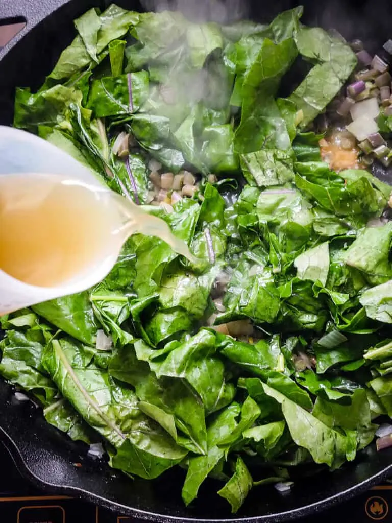 Image of chicken stock being poured into a skillet of kohlrabi greens.