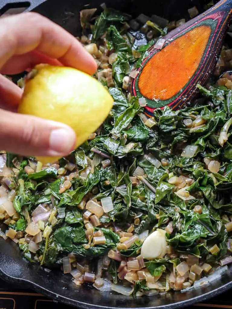 Image of a hand squeezing fresh lemon juice into a skillet of braised kohlrabi greens.