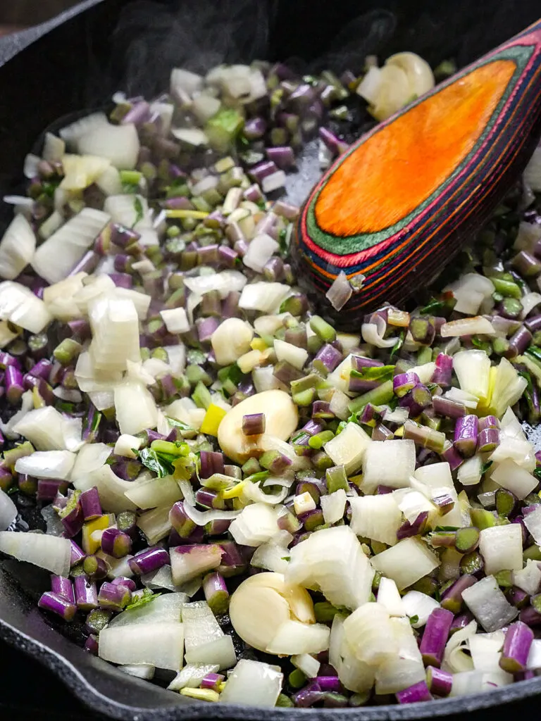 Close u of diced kohlrabi stems, onion, and garlic cloves cooking in a skillet.