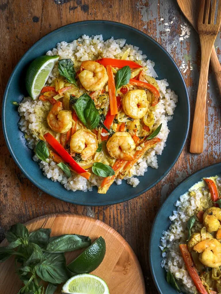 Stylized shot of Coconut Shrimp Curry on blue plates on a wooden table.