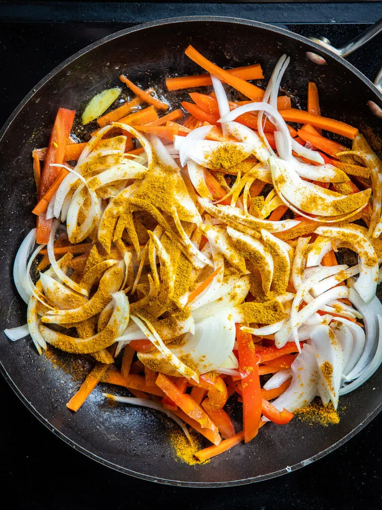 Sliced onions, red bell pepper, and carrots in a large skillet with curry powder.